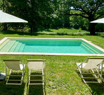 piscine avec une eau bleue entourée d'herbe avec transats blancs dépliés