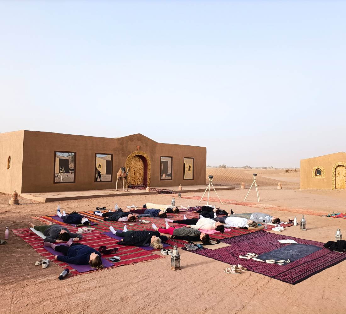 Voyageuse entrain de faire du yoga dans le désert au Maroc au lever du soleil